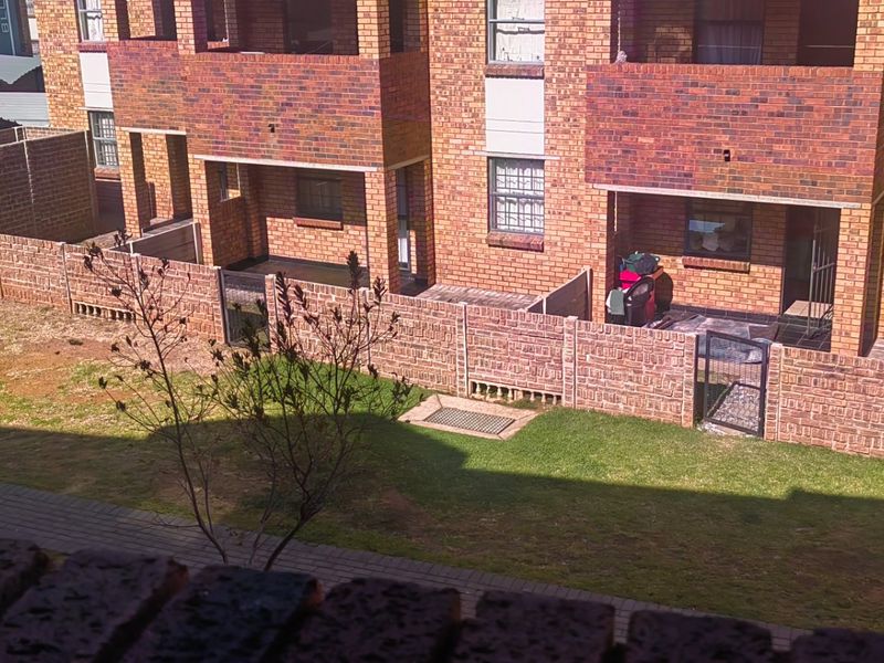An elevated view of the apartment complex rear exterior, featuring face brick facades, private paved patios, and a shared garden area with paved walkways.