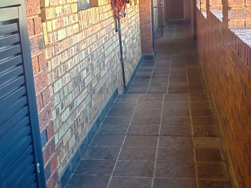 An exterior apartment hallway featuring exposed brick walls, stone tile flooring, and a wall-mounted fire hose reel.