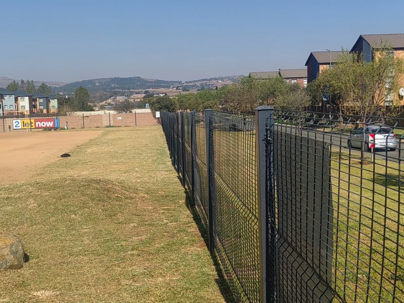An exterior view of the property grounds featuring secure perimeter fencing, adjacent road access, and open landscaped areas.