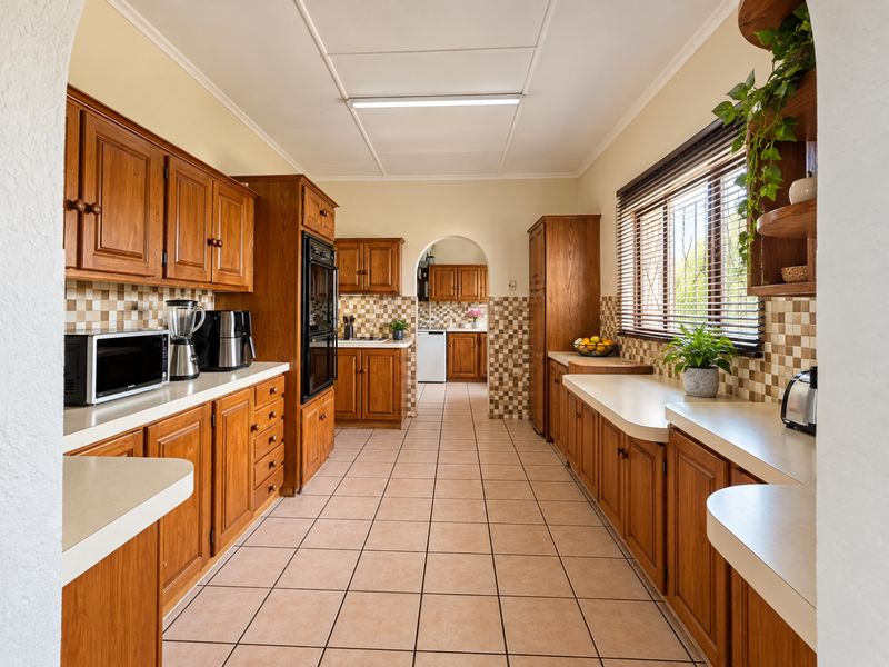 A spacious kitchen featuring traditional wooden cabinetry, tiled backsplash, and tiled flooring, with a functional layout and an archway leading to a secondary prep area.