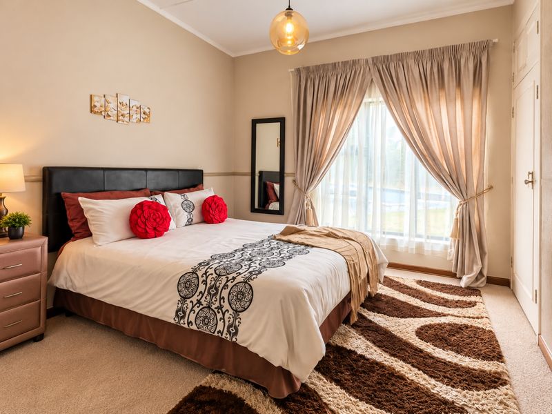 A well-maintained bedroom featuring neutral wall tones, carpeted flooring, a built-in cupboard, and a large window with elegant curtains.