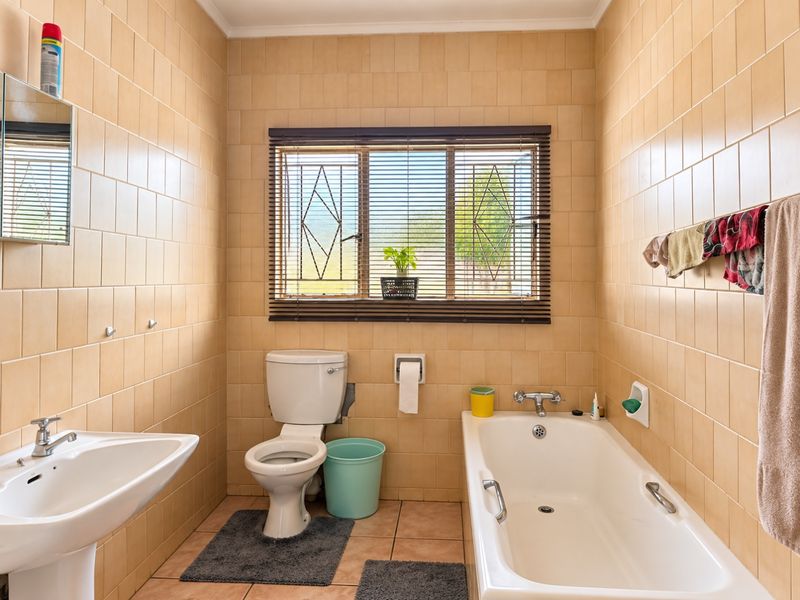 A functional bathroom featuring a pedestal basin, toilet, and bathtub with full-height wall tiling and a window with security bars.
