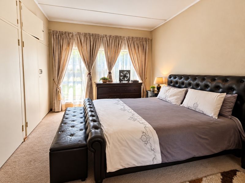 A comfortable bedroom featuring neutral walls, carpeted flooring, and ample built-in cupboard storage, offering a functional and well-maintained living space.