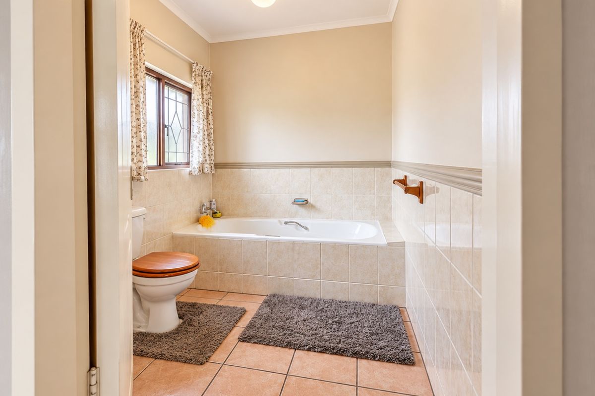 A functional bathroom featuring a built-in bathtub, ceramic tiling, and a toilet, with neutral wall finishes and a leaded glass window.