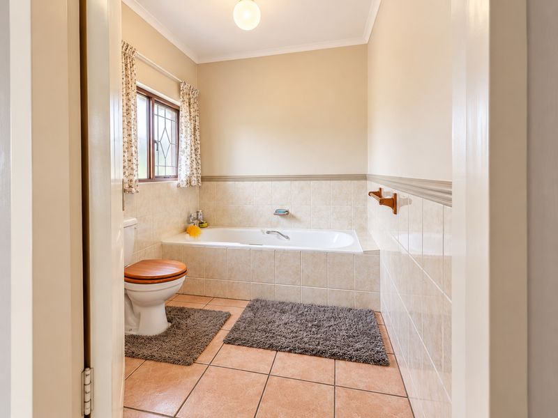 A functional bathroom featuring a built-in bathtub, ceramic tiling, and a toilet, with neutral wall finishes and a leaded glass window.