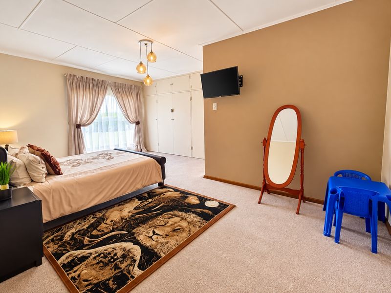 Spacious bedroom featuring neutral wall tones, carpeted flooring, and extensive built-in cupboard storage with large windows and curtain rails.