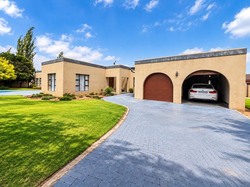 Front view of a single-story residence featuring a paved driveway, double garage with arched openings, and a well-maintained lawn.