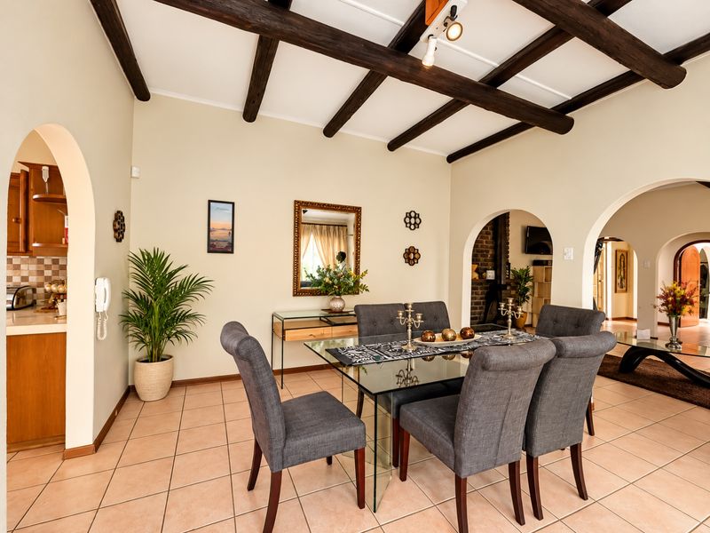Open plan dining area featuring exposed timber ceiling beams, tiled flooring, and arched architectural transitions leading to the kitchen and adjacent living spaces.