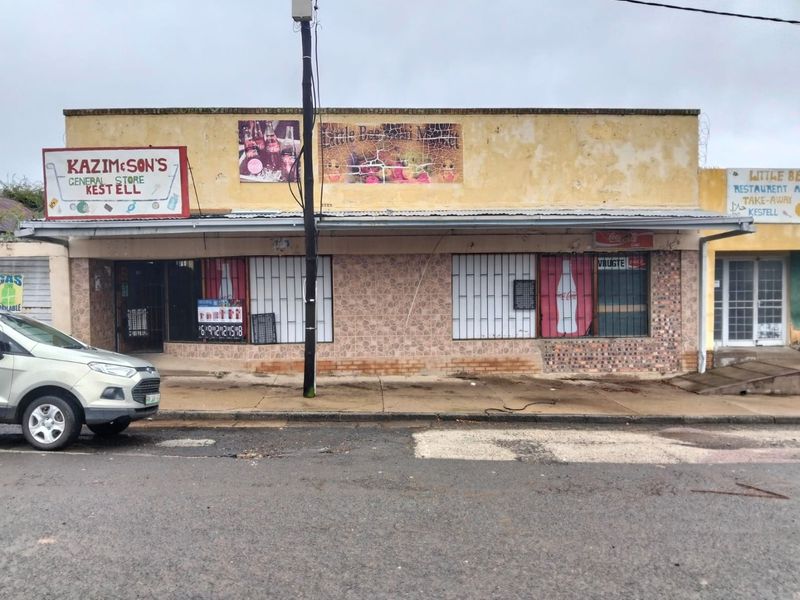 Commercial storefront featuring a covered walkway, metal security grilles, and tiled facade, currently showing signs of exterior weathering and wear.