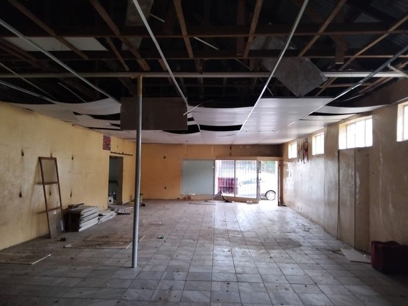 Vacant commercial open-plan space featuring tiled flooring, a metal support column, and significant ceiling damage requiring repair or replacement.