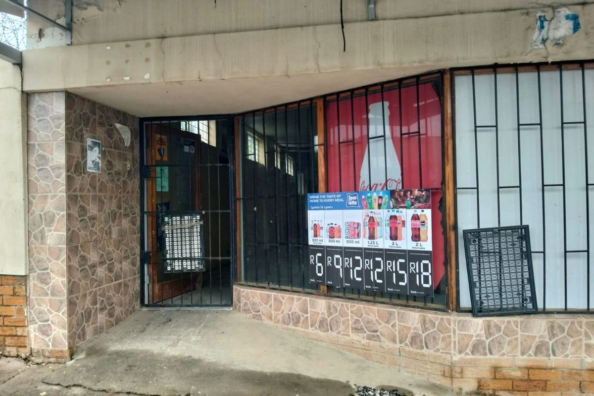 Commercial storefront entrance featuring stone cladding, security bars, and a concrete awning, showing signs of wear and weathering.