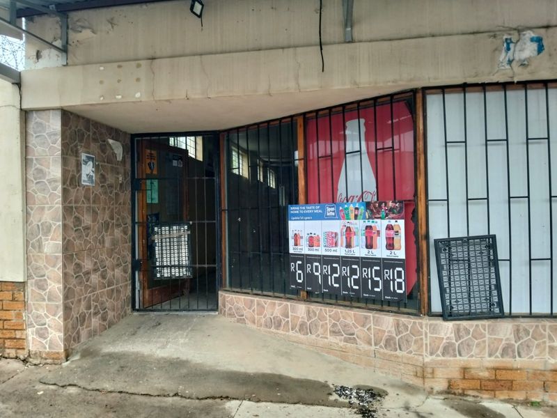 Commercial storefront entrance featuring stone cladding, security bars, and a concrete awning, showing signs of wear and weathering.