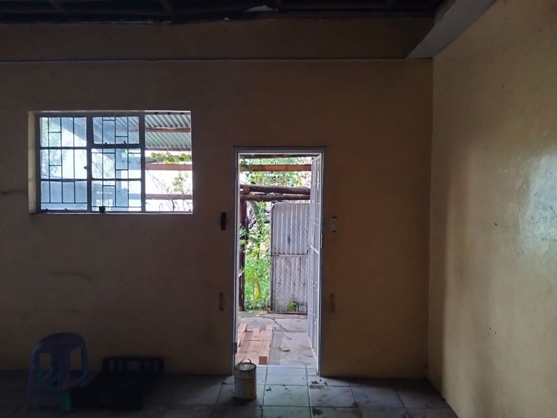 An empty, unfinished interior space featuring tiled flooring, a steel-framed window, and a security gate leading to an outdoor area.