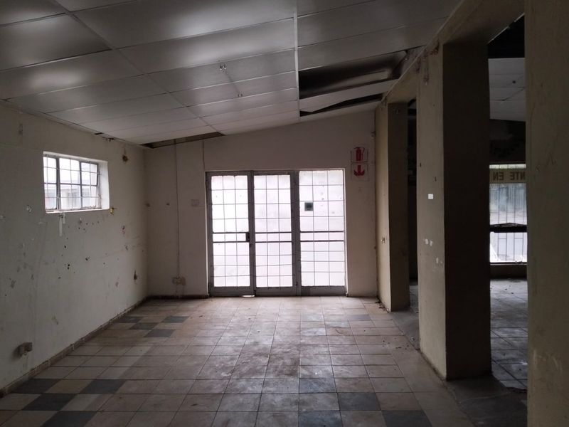 An empty, open-plan commercial space featuring tiled flooring, structural columns, and a suspended ceiling, requiring maintenance and cosmetic updates.