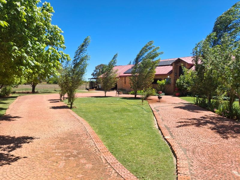 A well-maintained farm property featuring a circular brick driveway, landscaped garden, and a brick building with a metal roof and integrated solar panels.