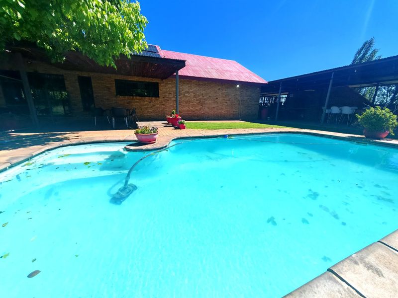 Outdoor pool area featuring a swimming pool, covered patio space, and brick building exterior with solar panels on the roof.