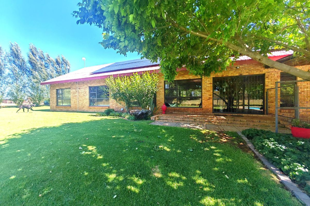 Rear view of a face brick farmhouse featuring a metal roof with solar panels, sliding glass doors, and a paved patio area overlooking the garden.