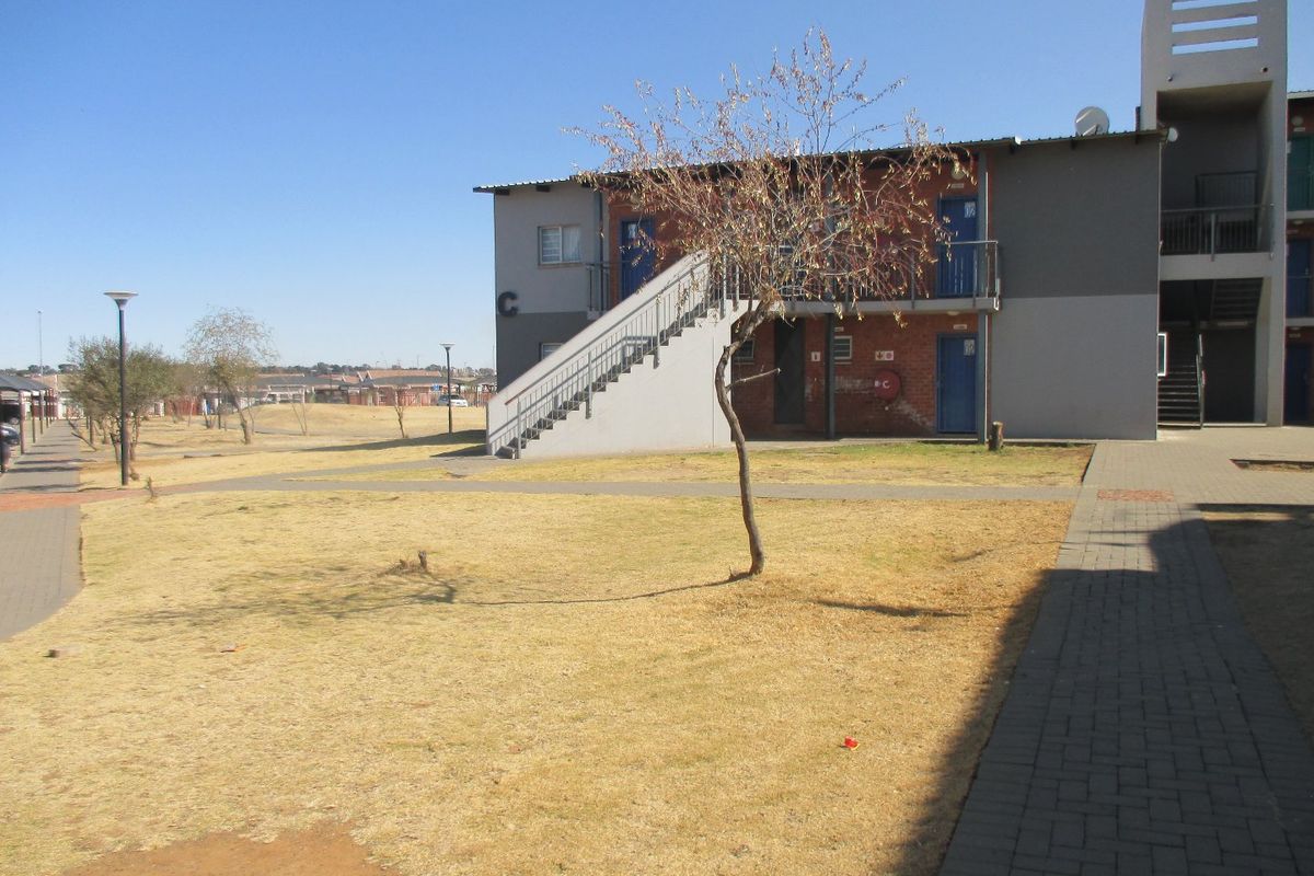 Exterior view of an apartment block featuring a paved walkway, external staircase, and communal garden area.