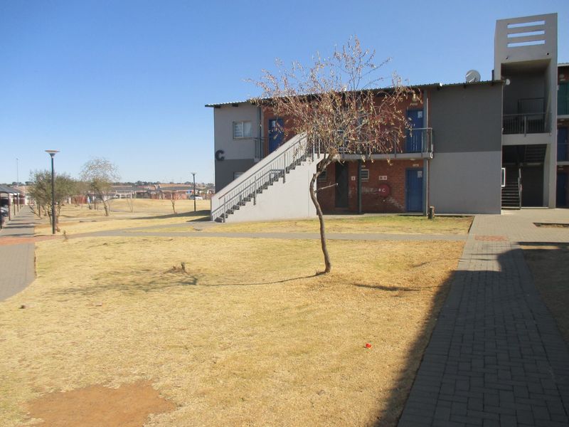 Exterior view of an apartment block featuring a paved walkway, external staircase, and communal garden area.