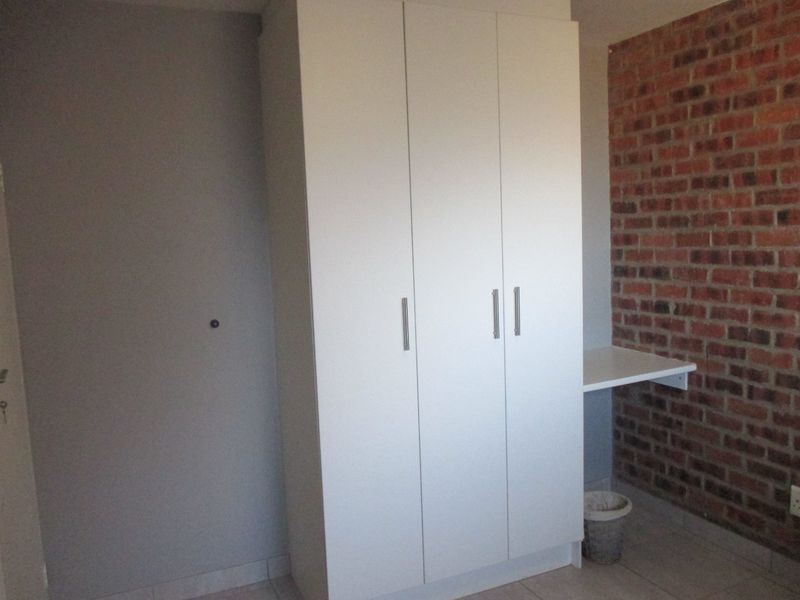A clean bedroom featuring a modern built-in wardrobe, a functional built-in desk, and a characterful exposed brick feature wall.