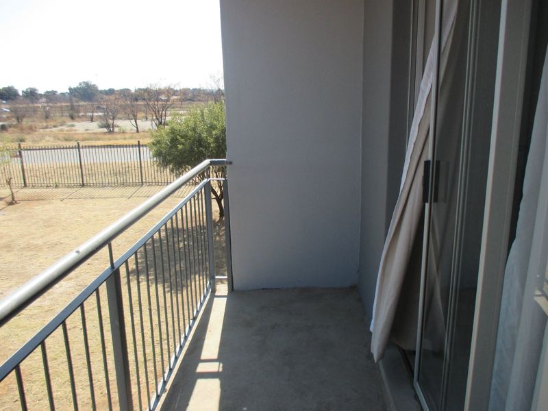 A simple balcony featuring a metal balustrade and sliding glass door access, overlooking an open field area.