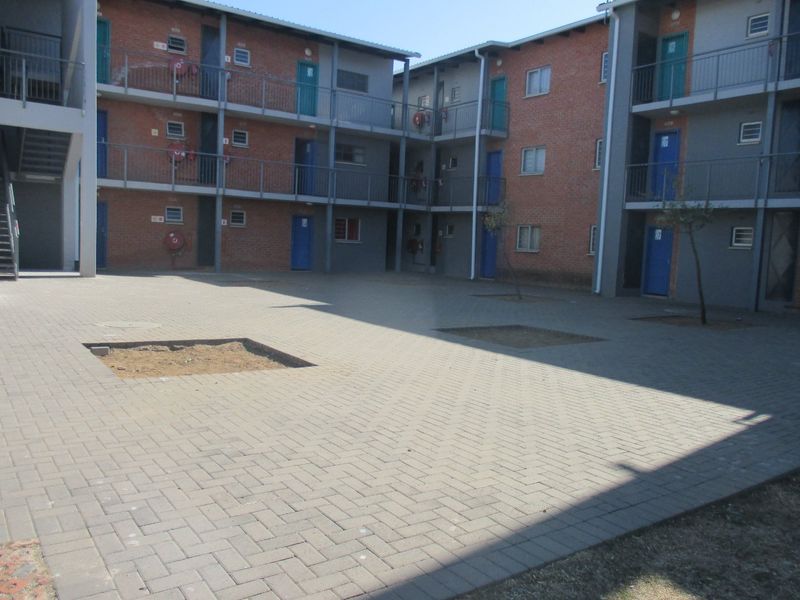 A view of the paved communal courtyard area between multi-story apartment blocks, featuring metal railings and external access stairwells.