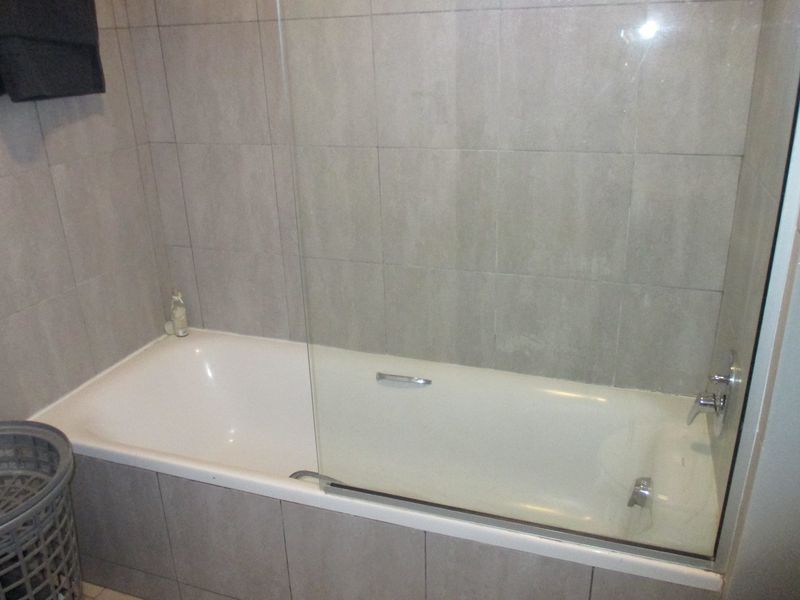 A functional bathroom featuring a bathtub with a glass shower screen and neutral wall tiling.