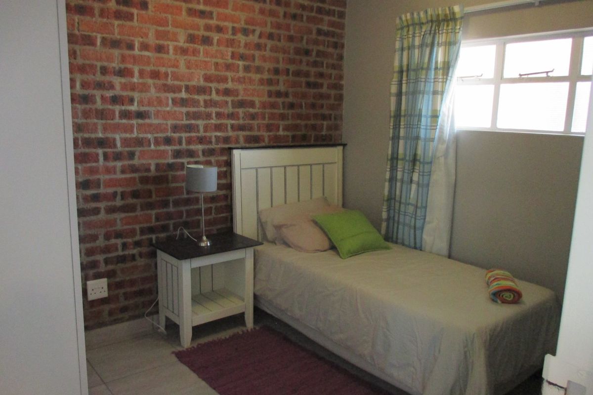 A cozy bedroom featuring an exposed brick accent wall, tiled flooring, and a functional casement window for natural light.