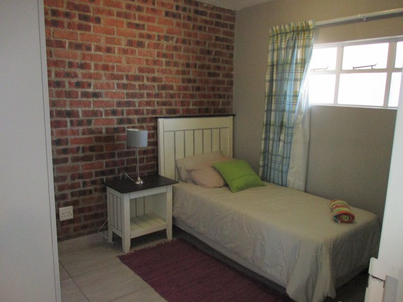 A cozy bedroom featuring an exposed brick accent wall, tiled flooring, and a functional casement window for natural light.