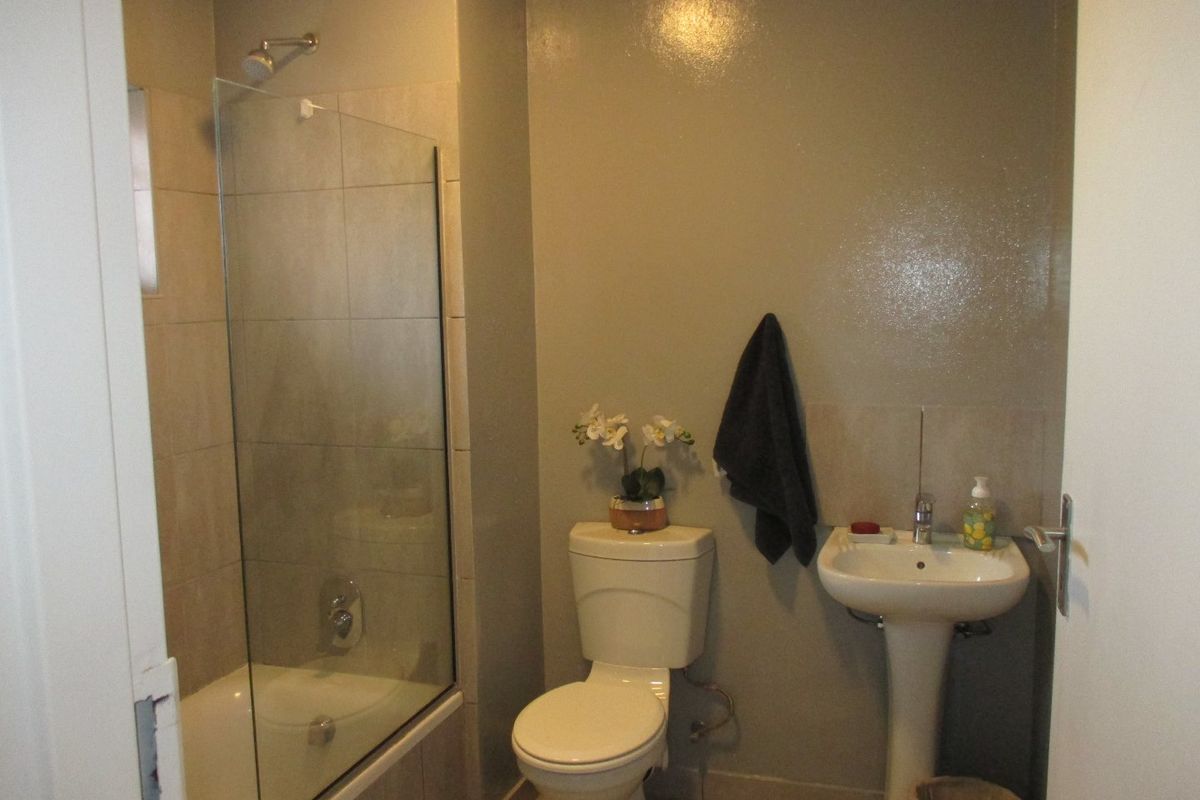 A functional bathroom featuring a shower-over-bath combination with a glass screen, a pedestal basin, and a standard toilet.