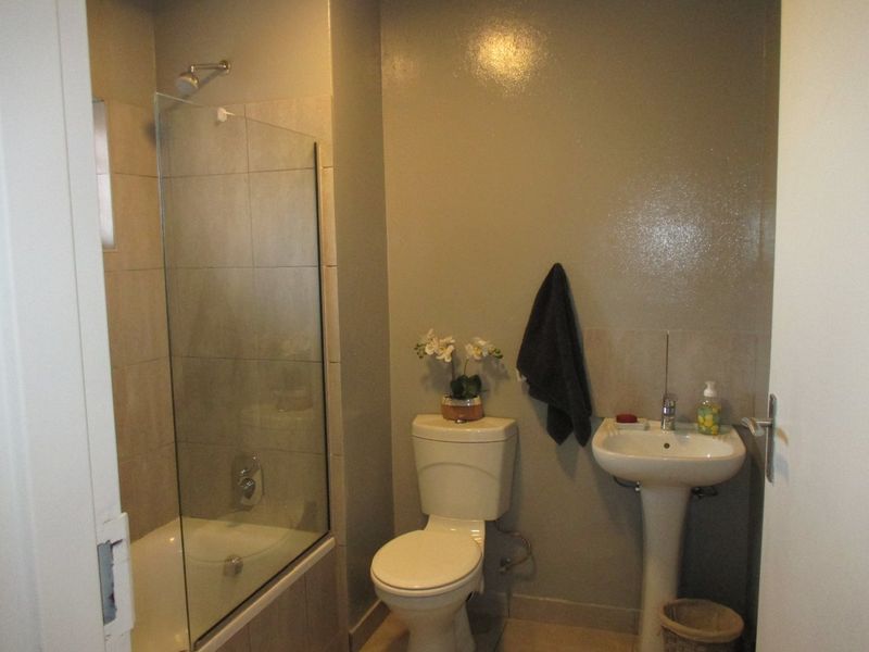 A functional bathroom featuring a shower-over-bath combination with a glass screen, a pedestal basin, and a standard toilet.