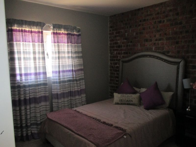 A bedroom featuring an exposed brick accent wall and a window with curtains.