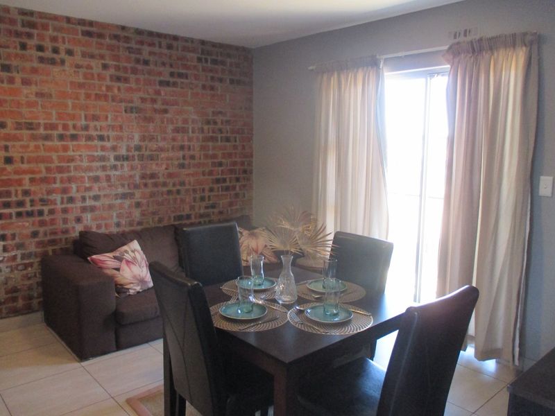 Open plan living and dining area featuring an exposed brick accent wall, tiled flooring, and access to a balcony through a sliding glass door.