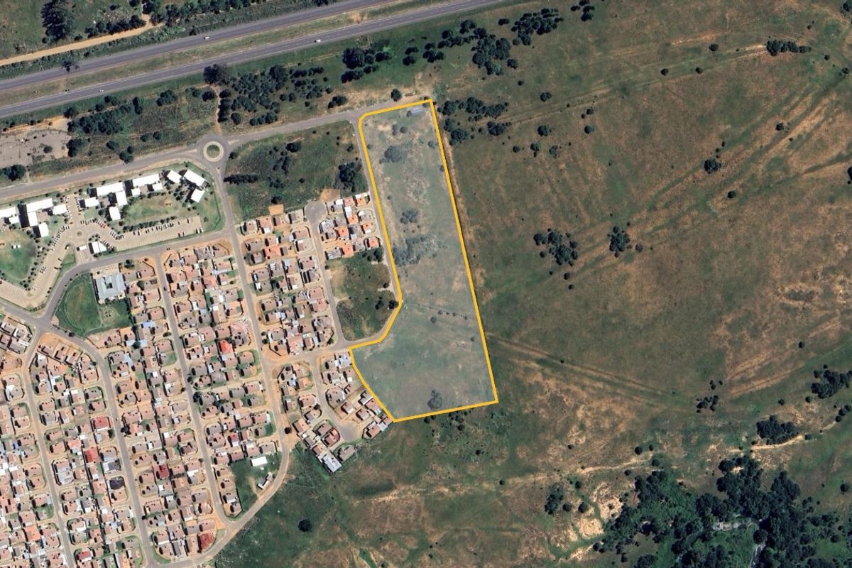 Aerial view of a vacant residential land parcel highlighted with boundary lines, situated adjacent to an existing residential development.