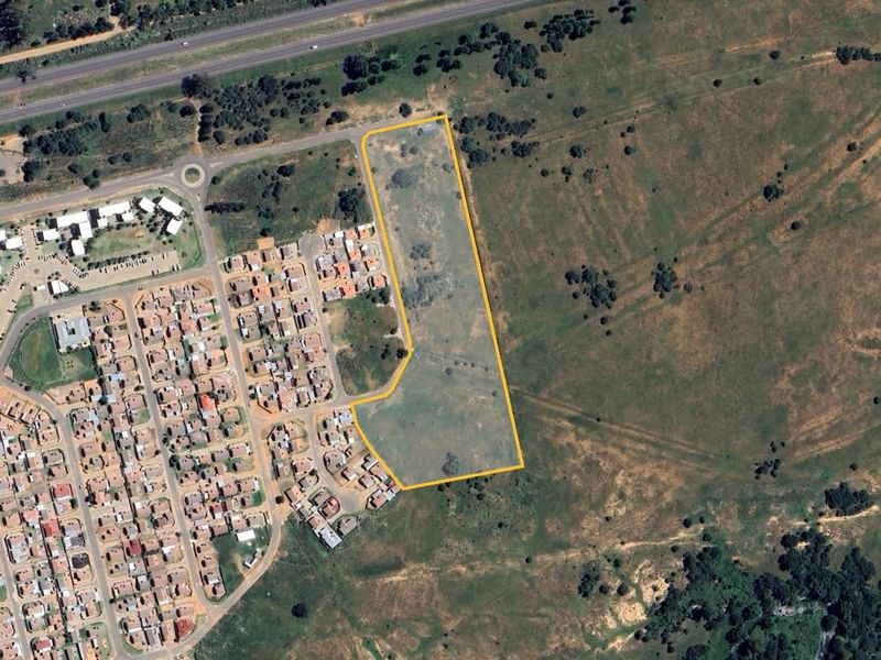 Aerial view of a vacant residential land parcel highlighted with boundary lines, situated adjacent to an existing residential development.