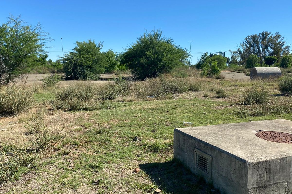 A view of a vacant residential plot featuring native vegetation and a concrete utility structure with a manhole cover.