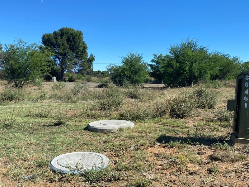 A vacant residential plot featuring natural vegetation, utility access points, and a street-facing utility box.