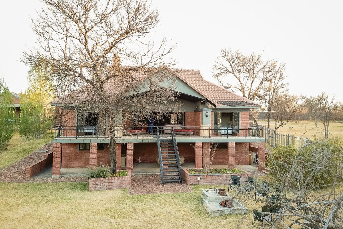 Rear view of a multi-level brick house featuring a raised patio, metal staircase, and a built-in fire pit in the garden area.