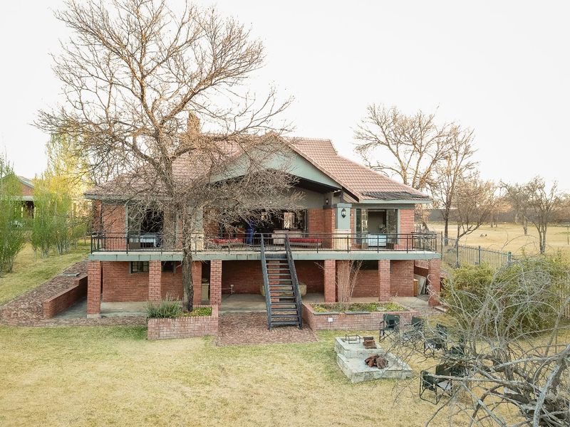Rear view of a multi-level brick house featuring a raised patio, metal staircase, and a built-in fire pit in the garden area.