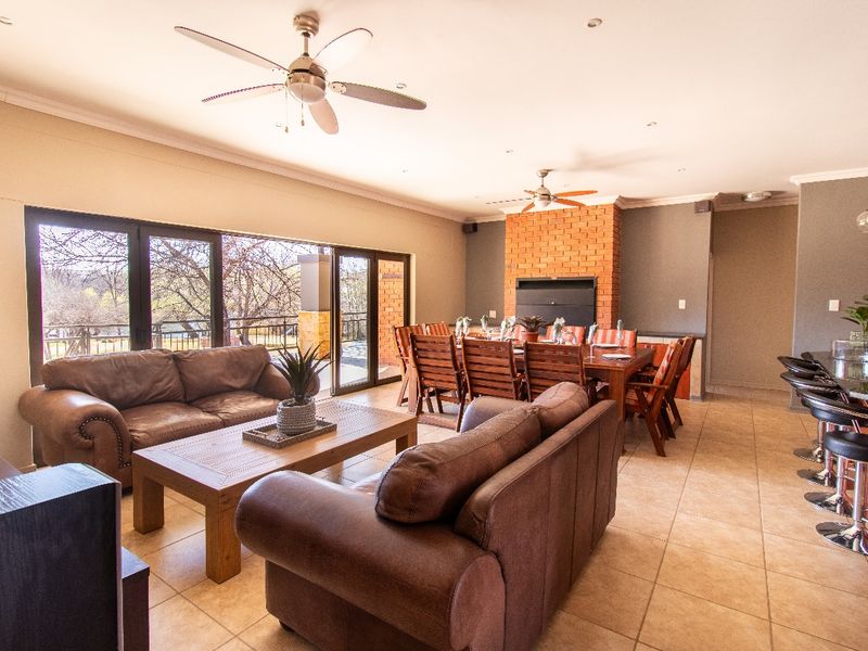 Spacious open-plan living and dining area featuring tiled floors, a brick fireplace with built-in braai, and large sliding doors leading to the patio.