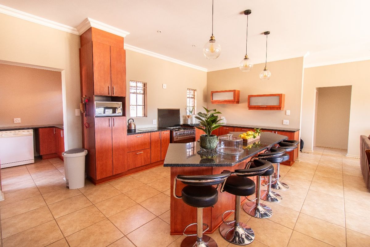 Spacious kitchen featuring wooden cabinetry, granite countertops, a central island with breakfast bar seating, and modern pendant lighting.