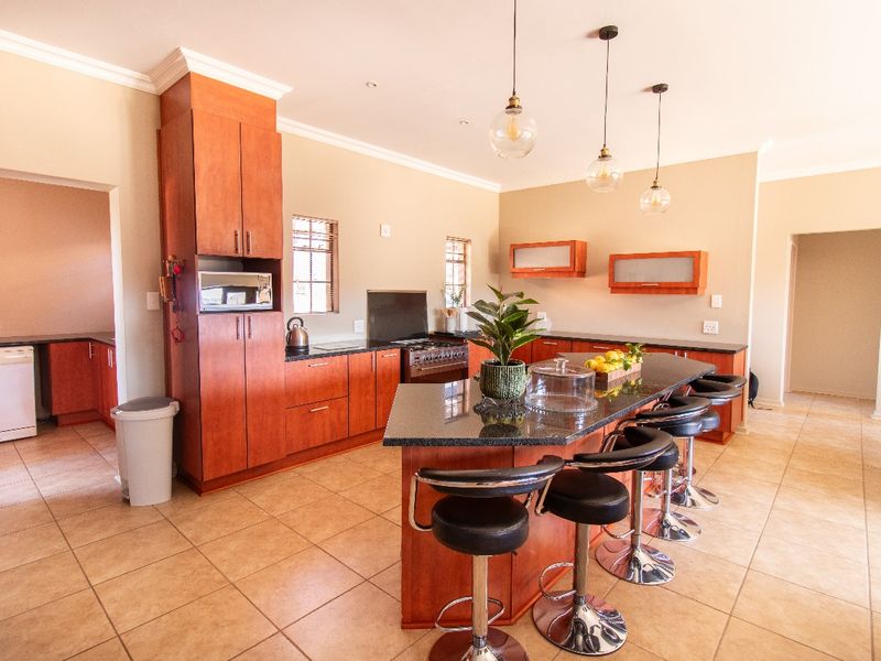 Spacious kitchen featuring wooden cabinetry, granite countertops, a central island with breakfast bar seating, and modern pendant lighting.