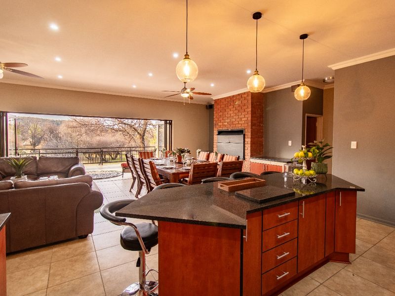 Spacious open-plan living and kitchen area featuring a central island, built-in fireplace with brick detail, and large stacking doors opening to an outdoor view.