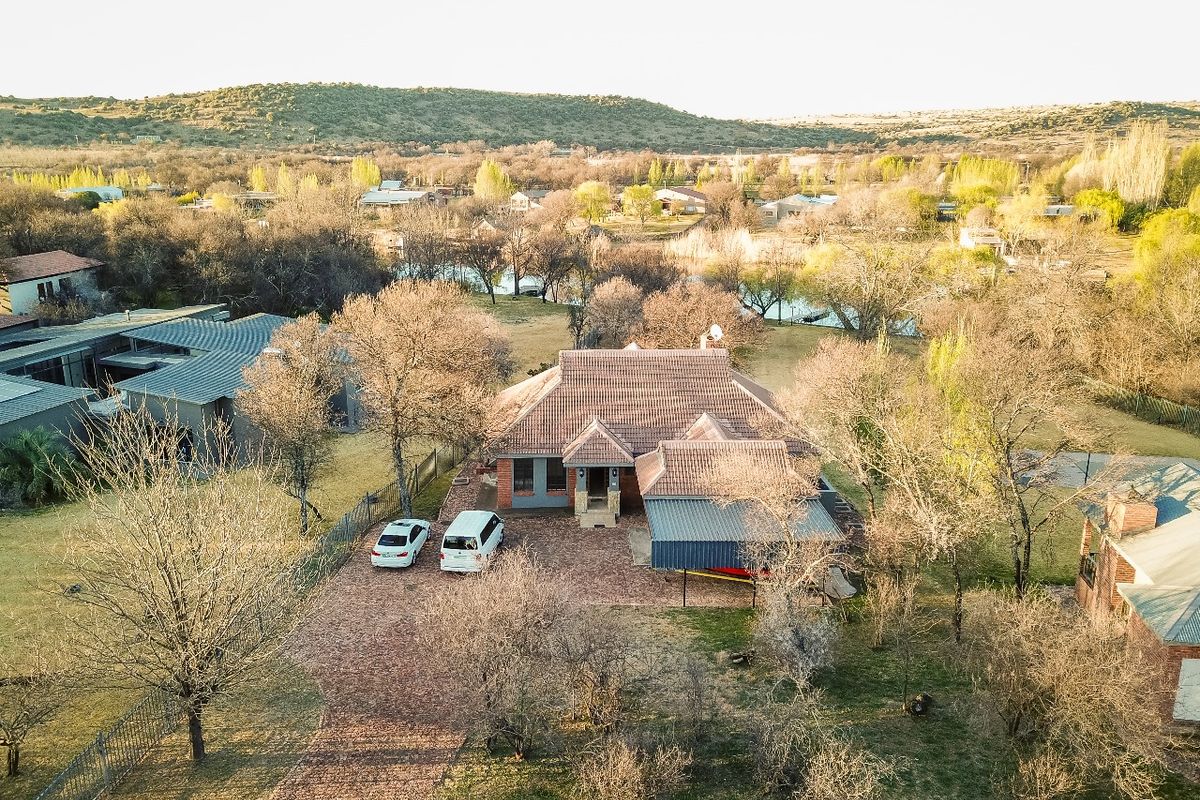 Aerial view of a residential property featuring a tiled roof house, brick driveway, and carport, set within a spacious landscaped garden area.