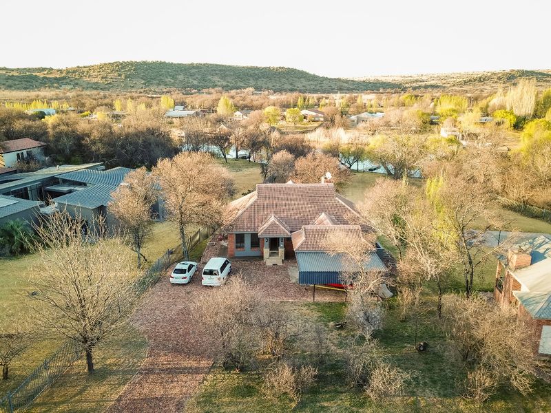 Aerial view of a residential property featuring a tiled roof house, brick driveway, and carport, set within a spacious landscaped garden area.