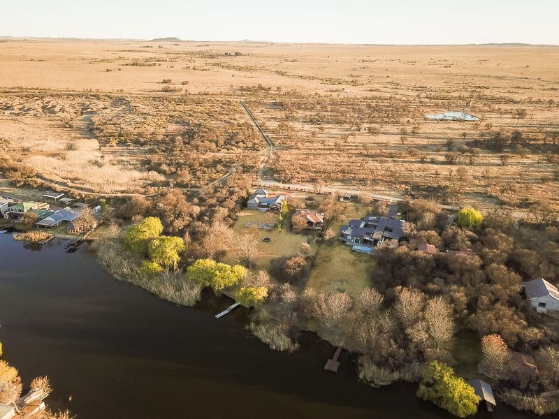 Aerial view of a waterfront property featuring a private jetty, swimming pool, and expansive landscaped grounds in a rural setting.