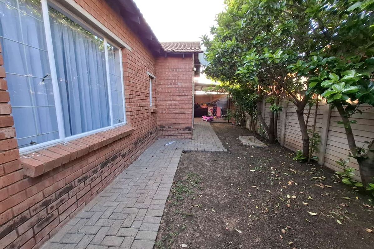A rear exterior view of the townhouse featuring a brick facade, a paved walkway, and a garden area enclosed by a precast concrete wall.
