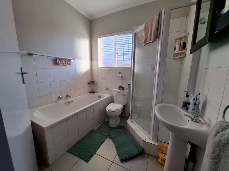 A functional bathroom featuring a bathtub, separate shower enclosure, pedestal sink, and toilet with neutral wall and floor tiling.