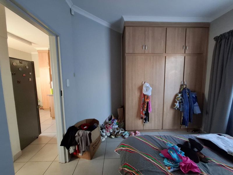 A bedroom featuring built-in wooden wardrobes, tiled flooring, and coving, with an adjacent view into a kitchen area.