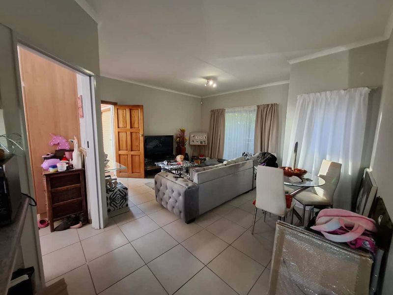 An open-plan living and dining area featuring neutral tiled flooring and direct access to an adjacent room through a timber door.